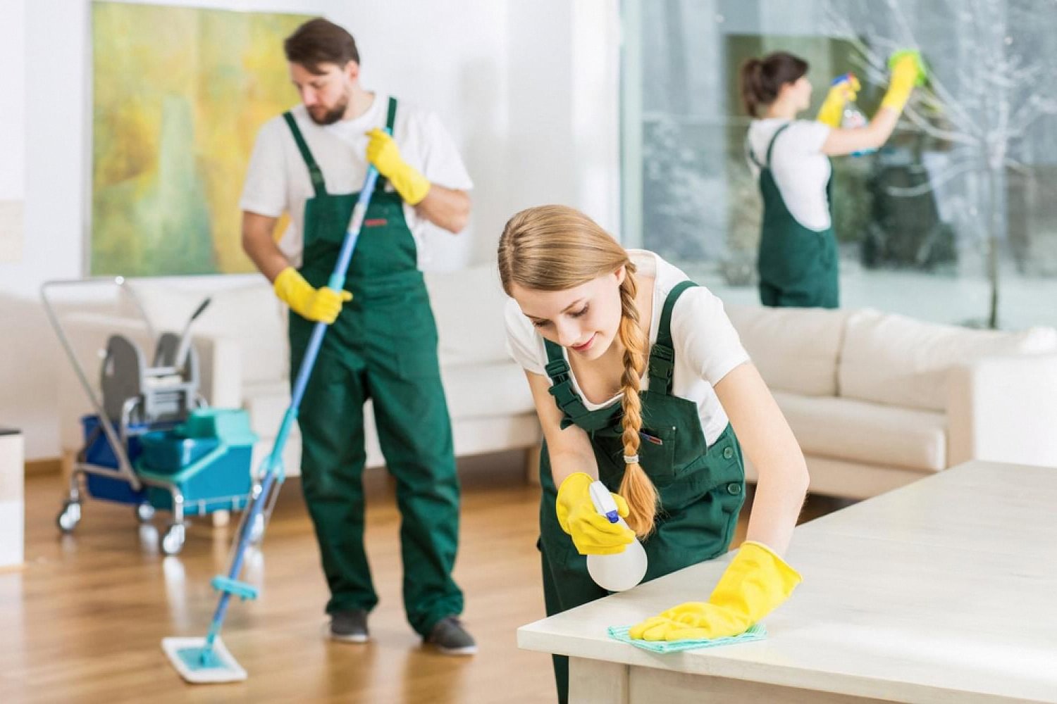 Two home maintenance technicians in green overalls cleaning a Dubai living room