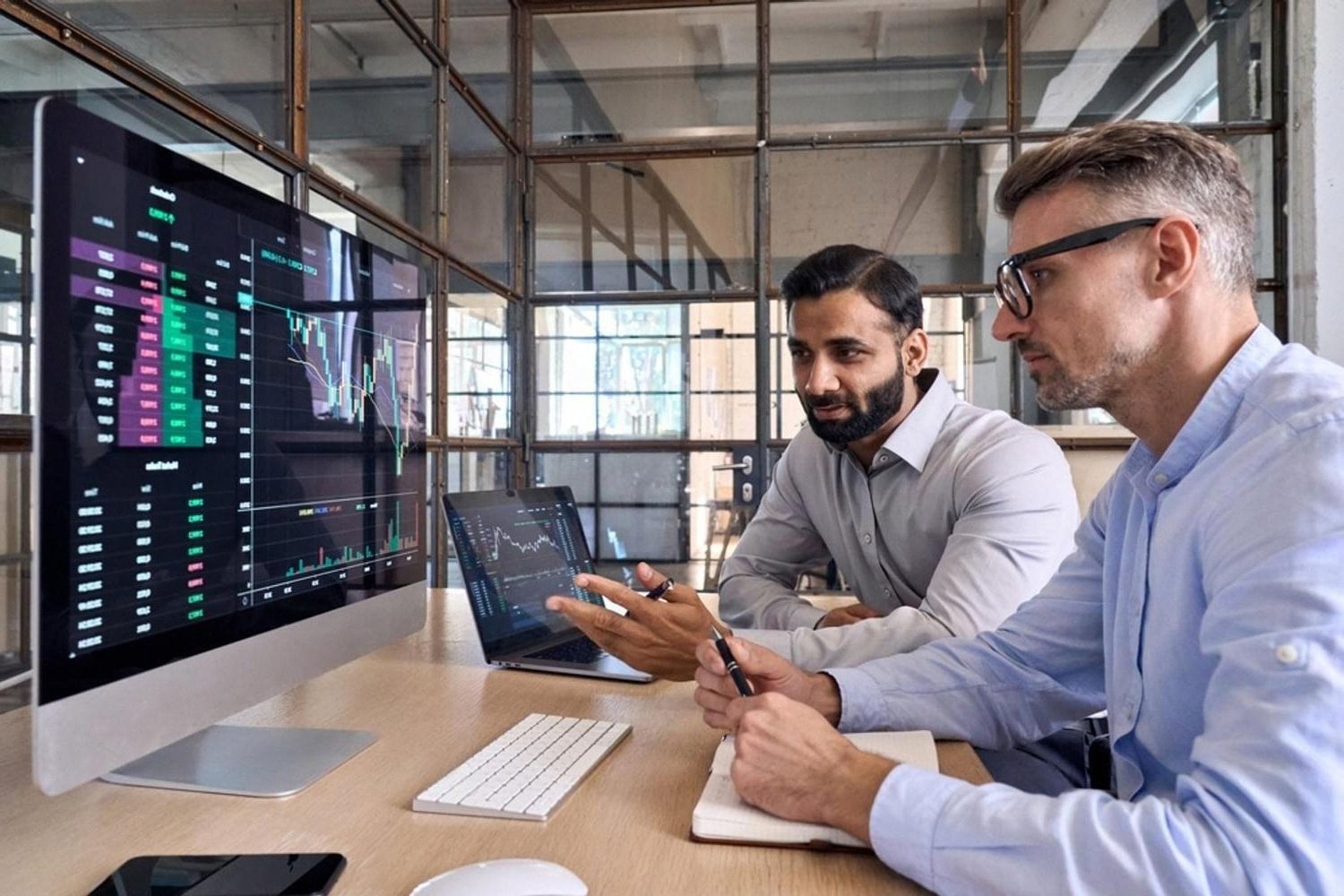Two analysts studying financial dashboards and operational risk data on large monitors